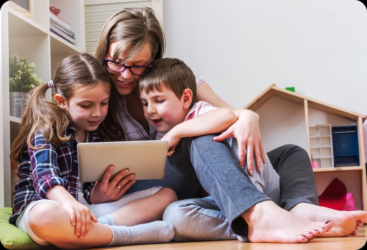 An adult and two children exploring a tablet together at home.
